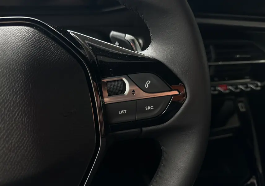 Gros plan sur les commandes gauche du volant en cuir noir du Peugeot 2008 gris Sellenium, avec touches téléphoniques et de liste.