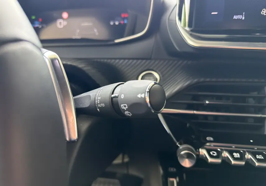 Gros plan intérieur sur la commande d’essuie-glace à gauche du volant du Peugeot 2008 gris Sellenium, avec tableau de bord numérique en arrière-plan.