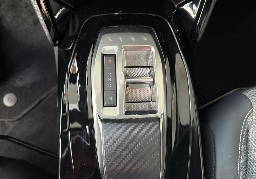 Vue plongeante sur la console centrale noire brillante du Peugeot 2008 1.2 130 EAT8 Allure avec sélecteur de boîte auto et finition carbone.