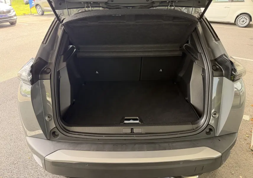 Coffre ouvert vu de l'arrière d'un Peugeot 2008 gris Sellenium, montrant un espace de chargement vide et propre.