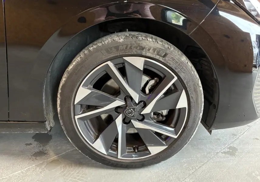 Gros plan sur la roue avant gauche noire d'une Peugeot 308 SW 2024 avec jante alliage 17'' Halong diamantée.