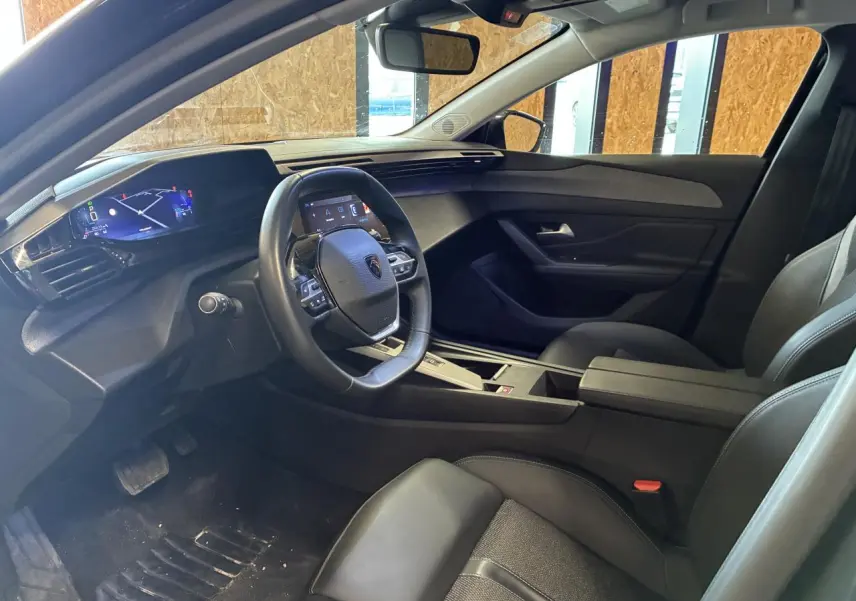 Intérieur Peugeot 308 SW 2024 vu côté conducteur, tableau de bord numérique et sellerie noire moderne.