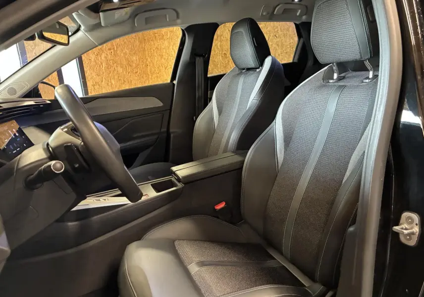 Vue intérieure côté conducteur de la Peugeot 308 SW noire, montrant les sièges avant en tissu et cuir avec accoudoir central.
