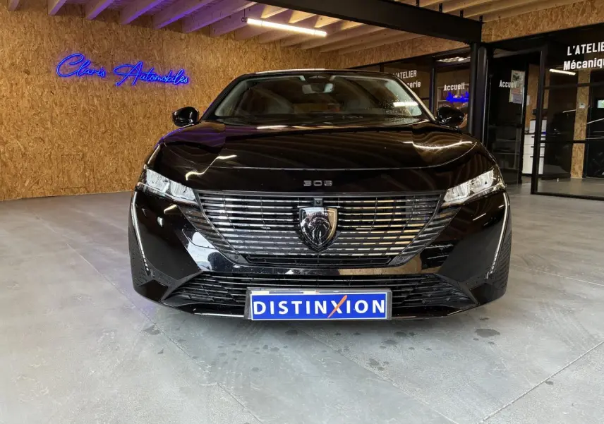 Vue avant d'une Peugeot 308 SW noire 2024 avec calandre chromée et logo lion au centre, en intérieur showroom.