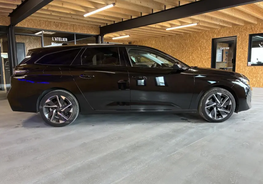 Peugeot 308 SW noire vue de profil côté gauche dans un garage avec jantes alliage et vitres surteintées.
