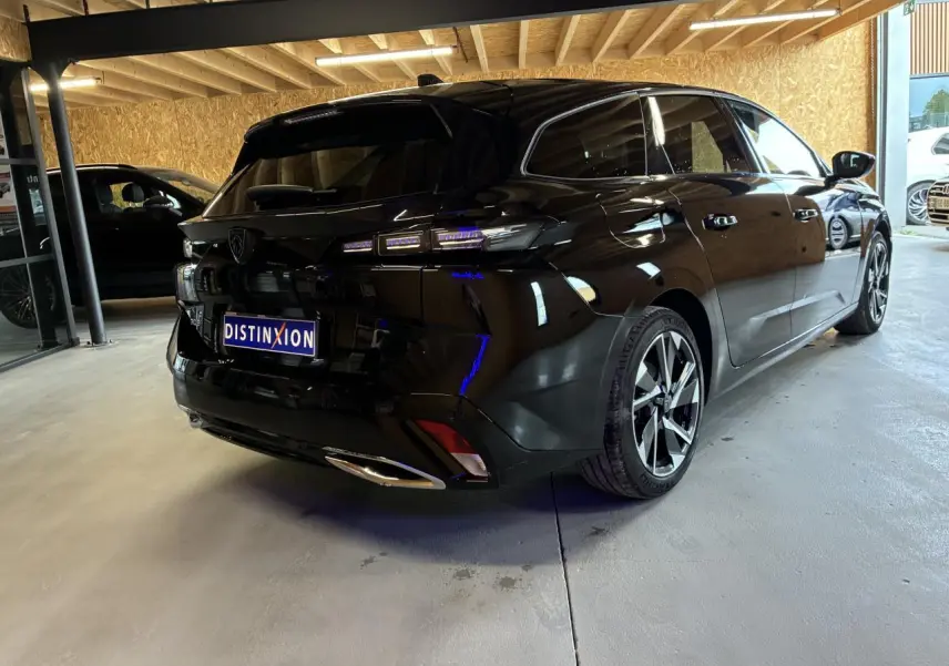 Peugeot 308 SW noire vue 3/4 arrière droit en intérieur avec jantes alliage et feux LED distinctifs.