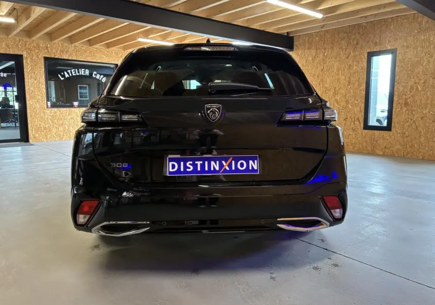 Vue arrière d'une Peugeot 308 SW noire 2024 avec feux LED et double sortie d'échappement chromée dans un garage.