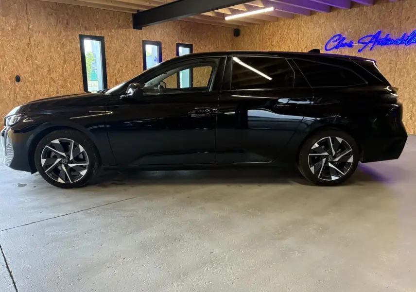 Peugeot 308 SW noire vue de profil gauche dans un garage avec jantes alliage et vitres surteintées.