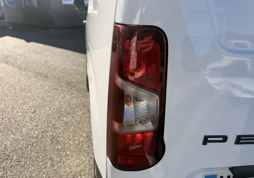 Gros plan sur le feu arrière droit d’un Peugeot Partner blanc, avec partie arrière et logo partiel visibles.