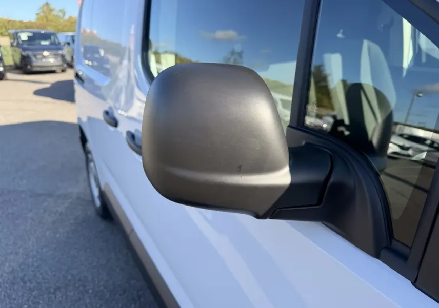 Vue rapprochée du rétroviseur côté conducteur d’un Peugeot Partner blanc, avec reflet du ciel bleu sur la carrosserie.