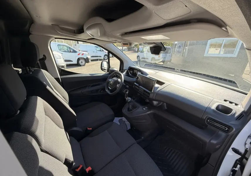 Vue intérieure côté conducteur du Peugeot Partner blanc, montrant le tableau de bord et les sièges avant noirs.
