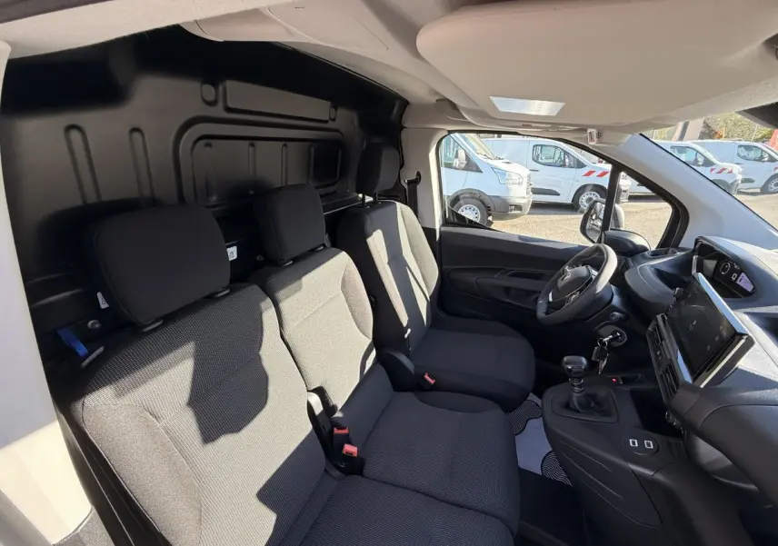 Intérieur avant du Peugeot Partner blanc 2026, vue côté droit montrant sièges tissu gris et tableau de bord moderne.
