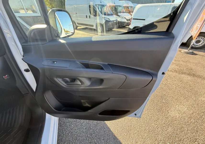 Vue intérieure de la porte côté conducteur du Peugeot Partner blanc, avec poignée et commande de vitre visible.