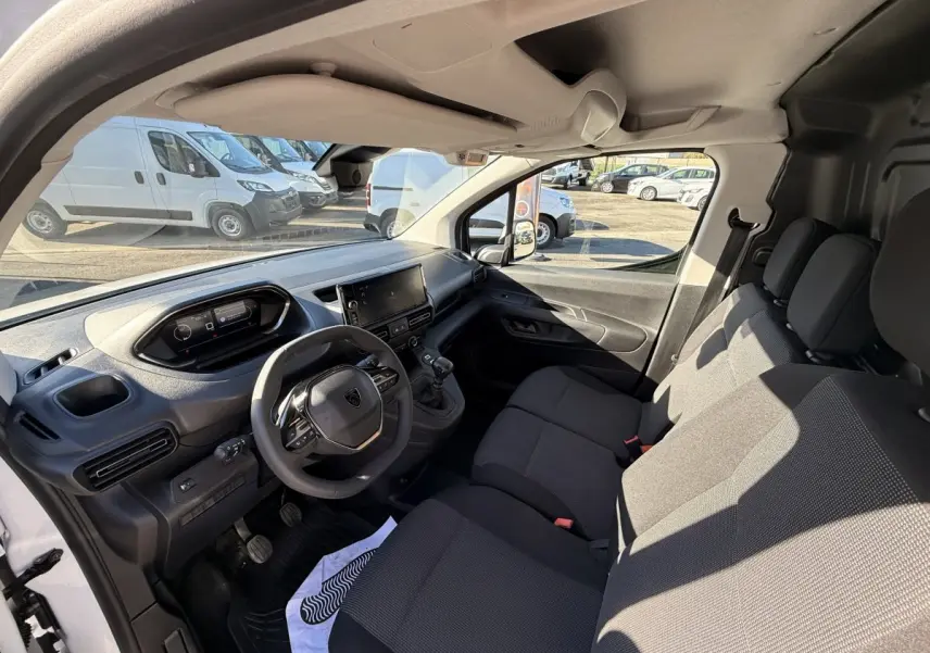 Vue intérieure côté conducteur du Peugeot Partner blanc 2026, montrant le tableau de bord et les sièges avant en tissu noir.