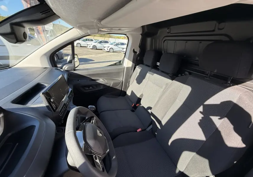 Vue intérieure avant droite du Peugeot Partner blanc 2026, montrant le volant multifonctions et la banquette trois places.