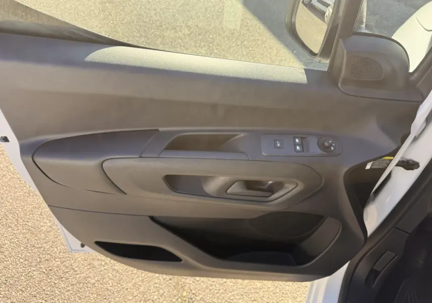 Vue intérieure de la porte avant gauche noire du Peugeot Partner blanc, avec commandes électriques des vitres et rétroviseurs.