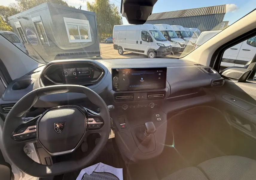 Vue intérieure du poste de conduite du Peugeot Partner blanc 2026, avec volant multifonctions et écran tactile central.
