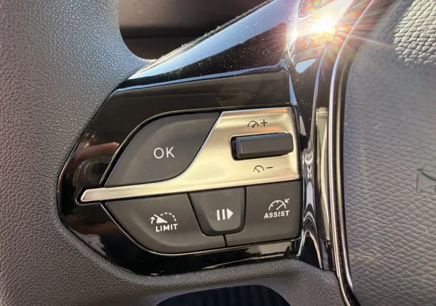 Gros plan sur les commandes noires et argentées du volant multifonctions du Peugeot Partner blanc, côté gauche.