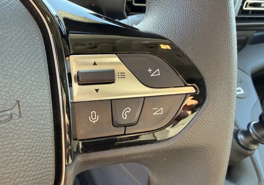 Gros plan sur les commandes multifonctions noires et argentées du volant du Peugeot Partner blanc, côté gauche.