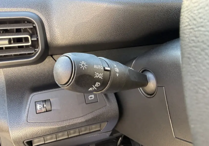 Gros plan sur la commande des phares à gauche du volant dans l’habitacle noir du Peugeot Partner blanc.