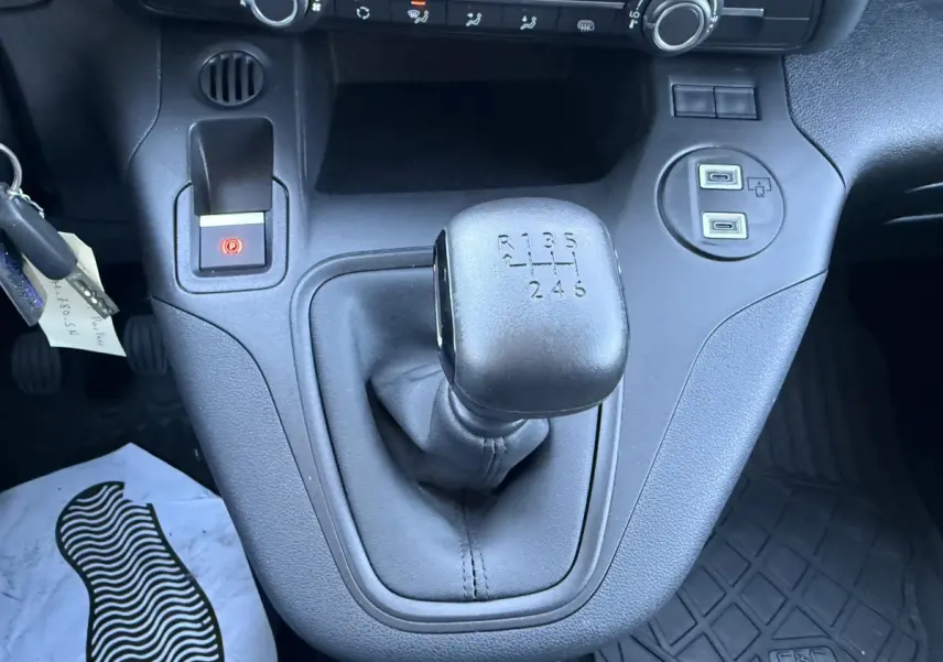 Gros plan intérieur sur le levier de vitesses manuel noir du Peugeot Partner blanc, avec ports USB et frein à main électrique.