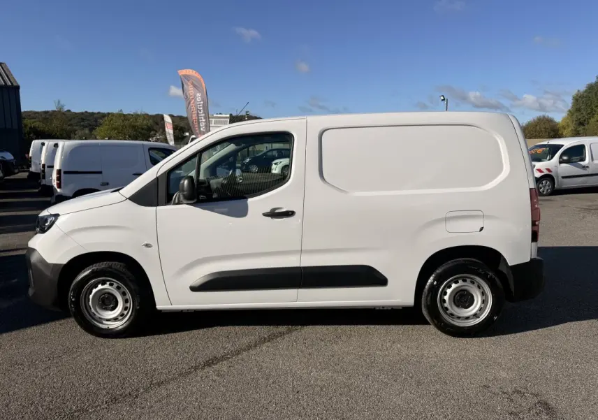 Vue de profil côté gauche d’un utilitaire Peugeot Partner blanc avec protections latérales noires sur un parking.