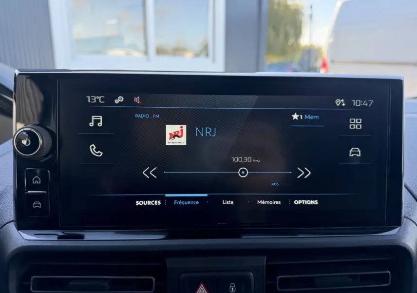 Écran tactile central du Peugeot Partner 2026 affichant la radio NRJ en FM, avec commandes tactiles sur le côté gauche.