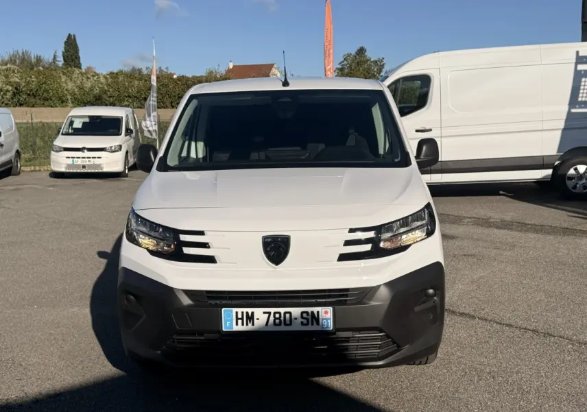 Vue de face d'un Peugeot Partner blanc avec pare-chocs noir, sur un parking en extérieur.