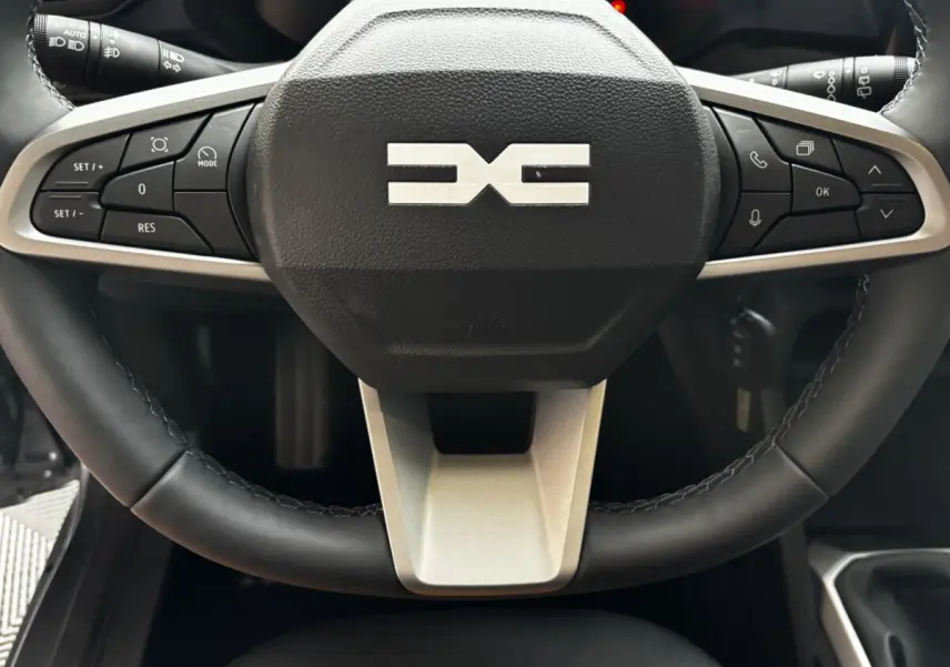 Gros plan sur le volant cuir noir du Dacia Bigster 2025 avec commandes multifonctions et logo central gris.