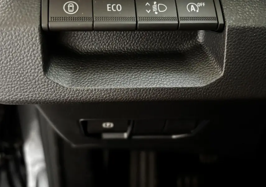 Gros plan sur les boutons de contrôle du tableau de bord du Dacia Bigster gris foncé, avec témoin orange allumé.