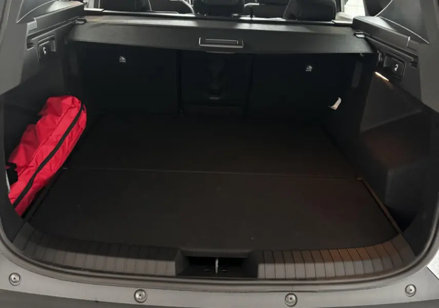 Coffre ouvert du Dacia Bigster gris foncé, vue arrière montrant la banquette arrière et un sac rouge à gauche.