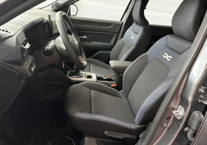 Intérieur avant droit du Dacia Bigster gris foncé, sièges tissu bi-ton avec logo DC et volant multifonctions.