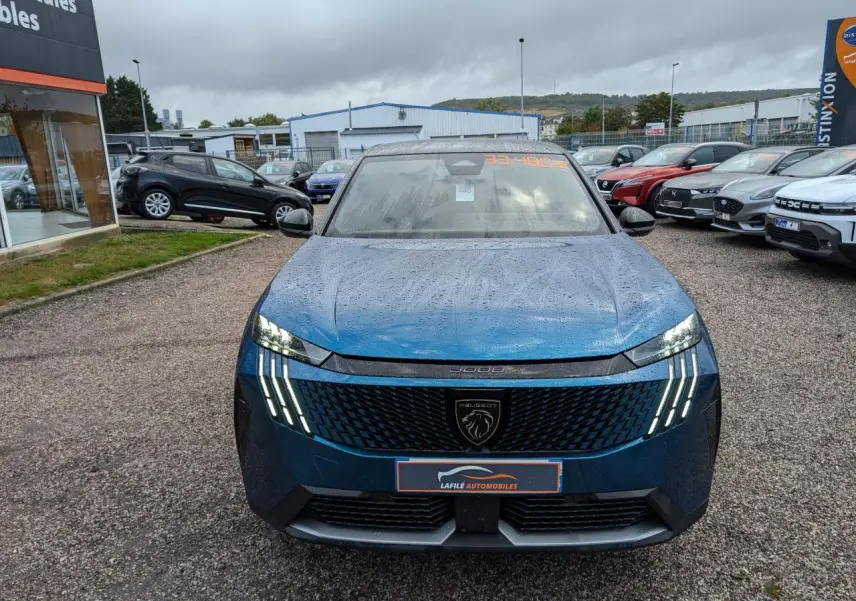Vue avant d'un Peugeot 3008 GT bleu métallisé avec feux LED griffes et calandre noire laquée sous un ciel nuageux.