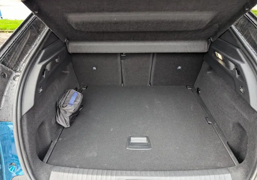 Coffre ouvert d’un Peugeot 3008 GT bleu métallisé, montrant un espace de rangement noir avec trousse sur le côté.