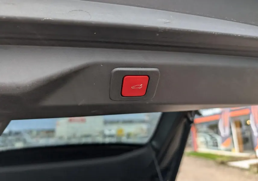 Bouton rouge d'ouverture électrique du hayon visible en gros plan sur un Peugeot 3008 hybride 2025.