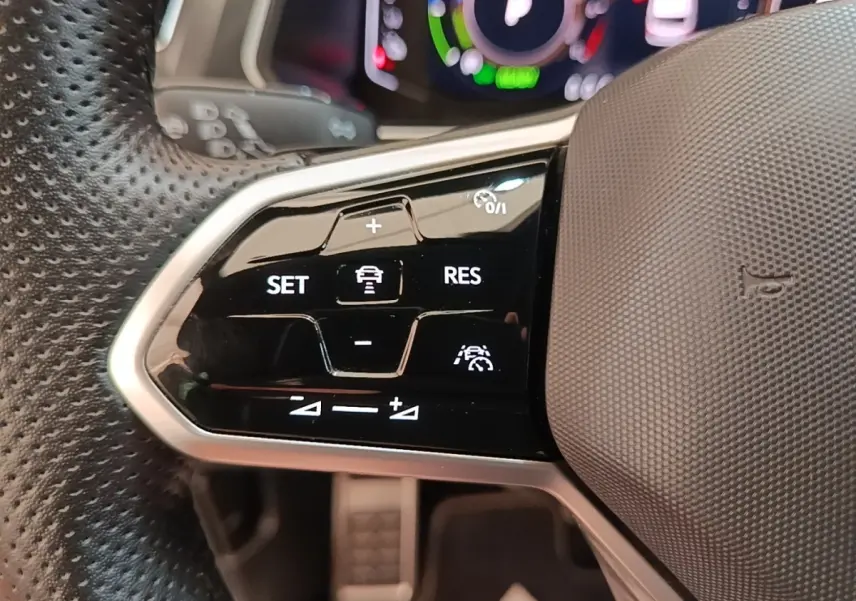 Gros plan sur les commandes de régulateur de vitesse au volant cuir perforé du Volkswagen Tiguan blanc 2023.