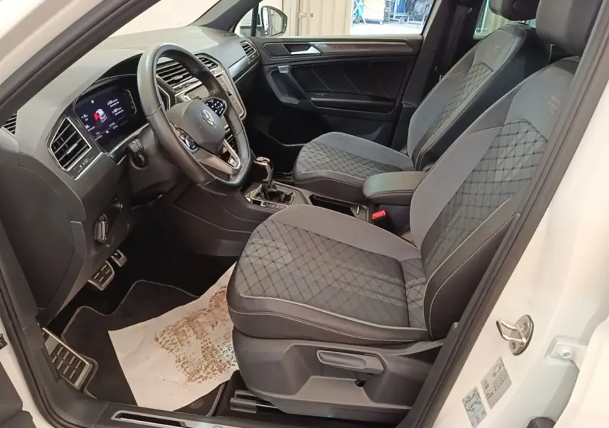 Vue intérieure côté conducteur du Volkswagen Tiguan blanc 2023, sièges R-Line avec surpiqûres et volant cuir multifonctions.