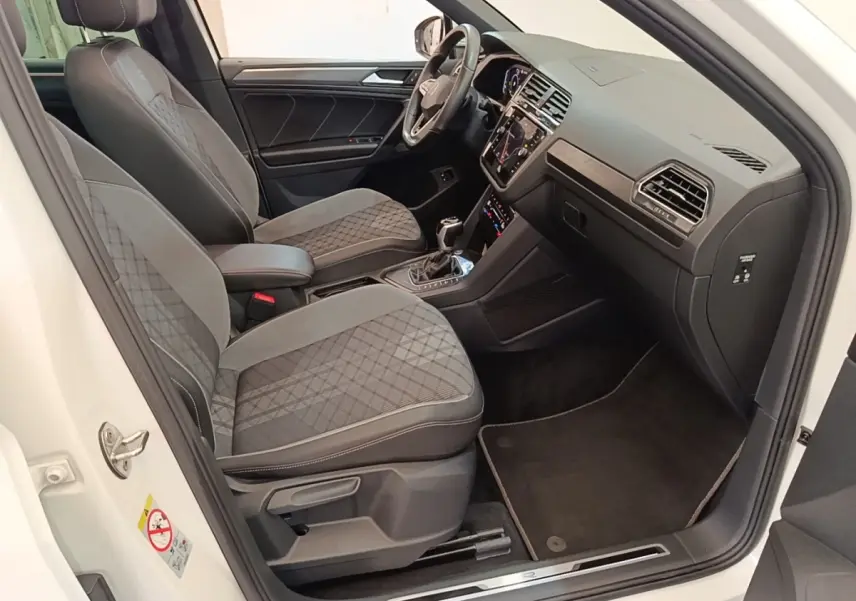 Intérieur avant droit du Volkswagen Tiguan blanc 2023, sièges tissu gris à motifs, tableau de bord moderne avec écran tactile.
