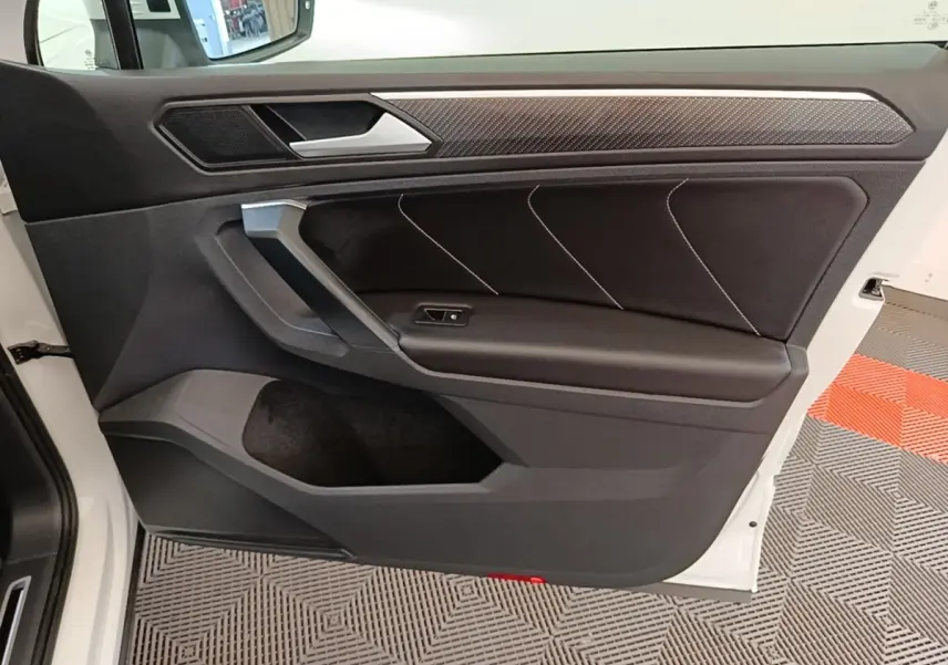 Vue intérieure de la porte avant gauche du Volkswagen Tiguan blanc, avec garniture noire et insert effet carbone.