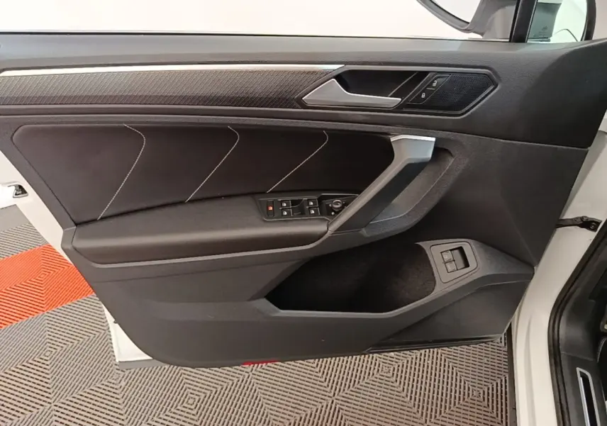 Vue intérieure côté gauche de la porte avant d’un Volkswagen Tiguan blanc avec garniture noire et commandes électriques.