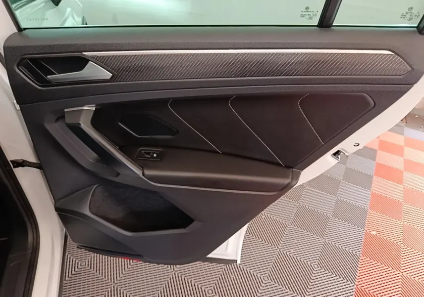 Vue intérieure de la porte arrière gauche du Volkswagen Tiguan blanc 2023 avec garniture noire et surpiqûres blanches.