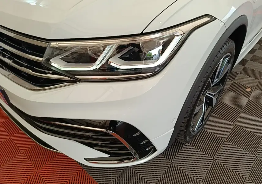 Gros plan sur l'avant droit blanc du Volkswagen Tiguan 1.4 eHybrid 2023, mettant en valeur le phare LED et la jante alliage.