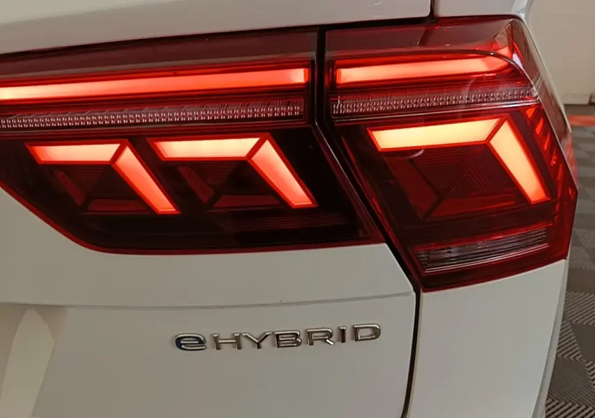 Gros plan sur le feu arrière droit rouge allumé du Volkswagen Tiguan blanc avec logo eHYBRID visible.
