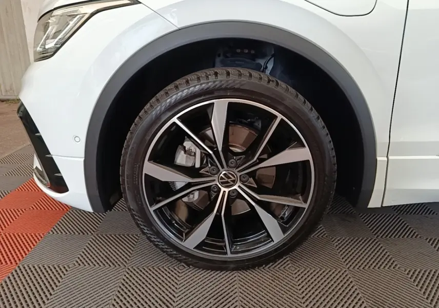 Gros plan sur la roue avant gauche du Volkswagen Tiguan blanc 2023 avec jante alliage noir et argent R-Line.