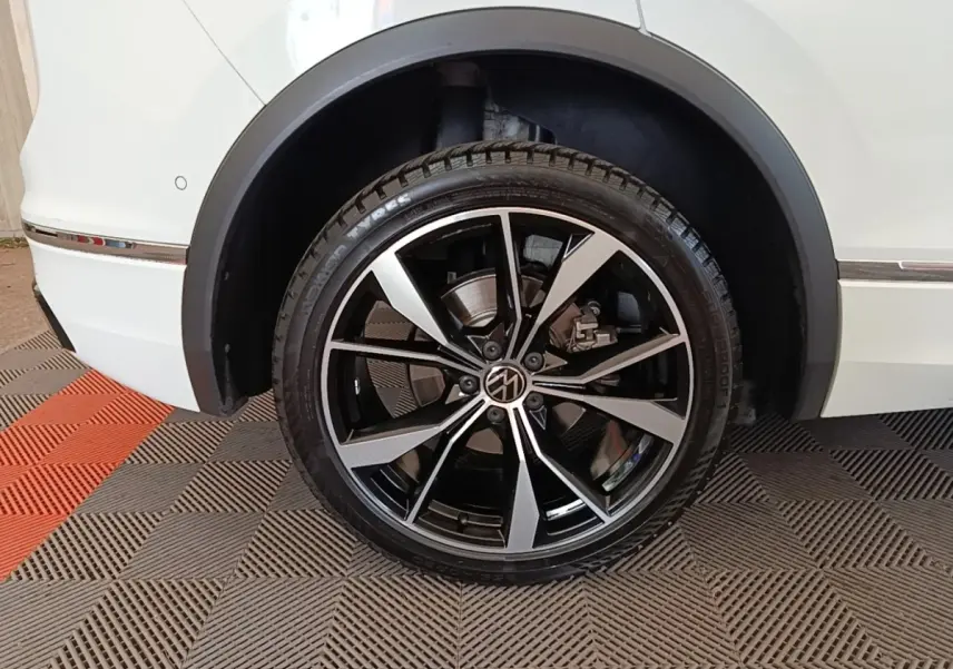 Gros plan sur la roue arrière droite du Volkswagen Tiguan blanc 2023 avec jante alliage noir et argentée R-Line.