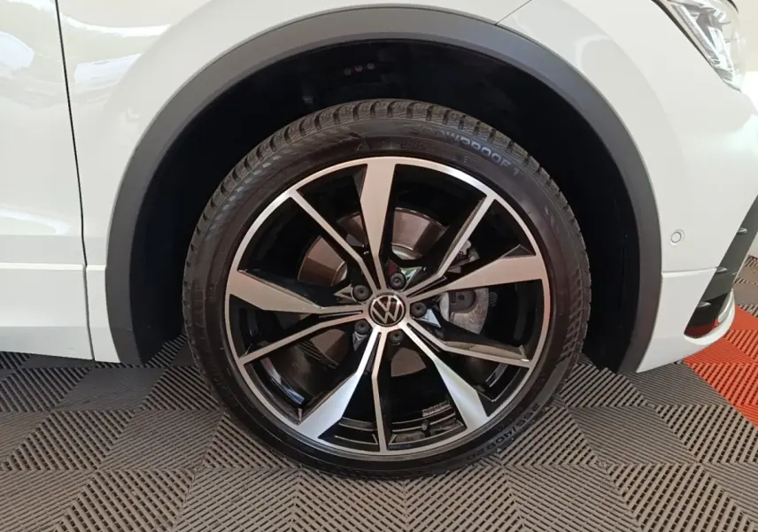 Gros plan sur la roue avant gauche du Volkswagen Tiguan blanc 2023 avec jante alliage R-Line noire et argentée.