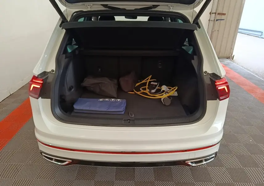 Vue arrière du coffre ouvert d’un Volkswagen Tiguan blanc 1.4 eHybrid 2023 avec câbles de recharge visibles.
