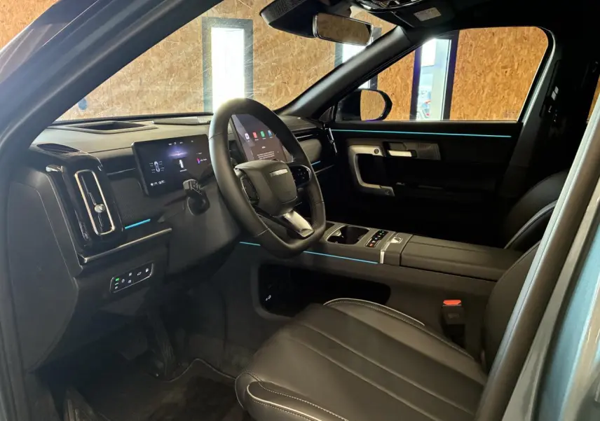 Vue intérieure côté conducteur du JAECOO J7 2026, sellerie cuir noir avec éclairage d'ambiance bleu subtil.