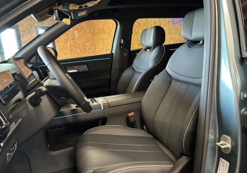 Vue intérieure côté conducteur du JAECOO J7 2026, sièges cuir noir avec surpiqûres blanches et éclairage d'ambiance bleu.