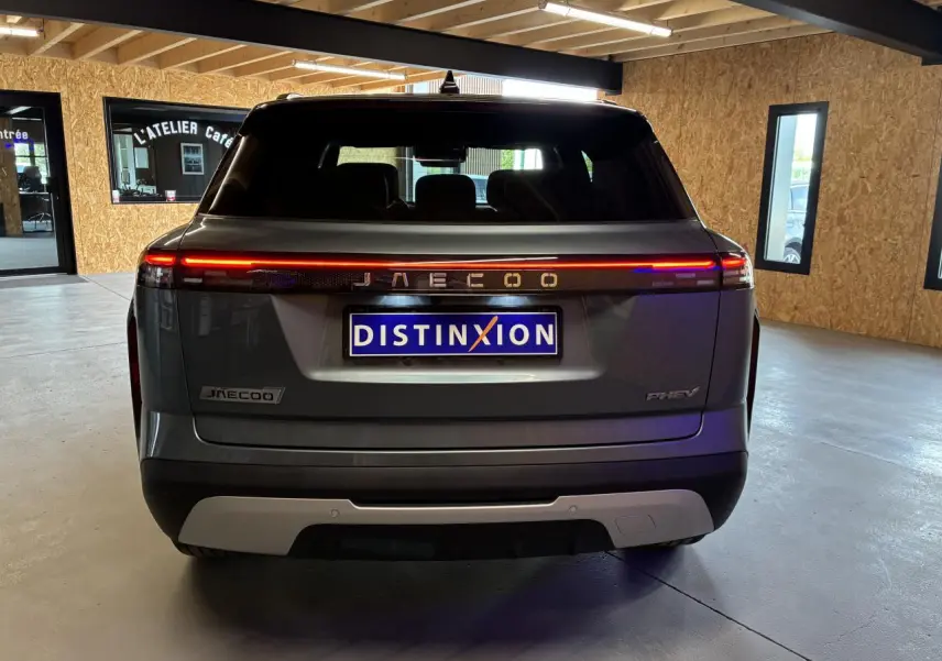 Vue arrière du SUV JAECOO J7 gris olive avec bandeau lumineux rouge et logo lumineux dans un garage.